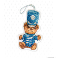 Een ornament versierd met kruissteken uit ons kostbare Luca-s borduurpakket, met een afbeelding van een teddybeer verkleed als koninklijke wacht. De beer draagt een blauw uniform met witte knopen en een hoge blauwe hoed versierd met een wit embleem. Aan de bovenkant is een gevlochten koord bevestigd om op te hangen. De achtergrond is een wit vlak met een subtiel stippenpatroon.
