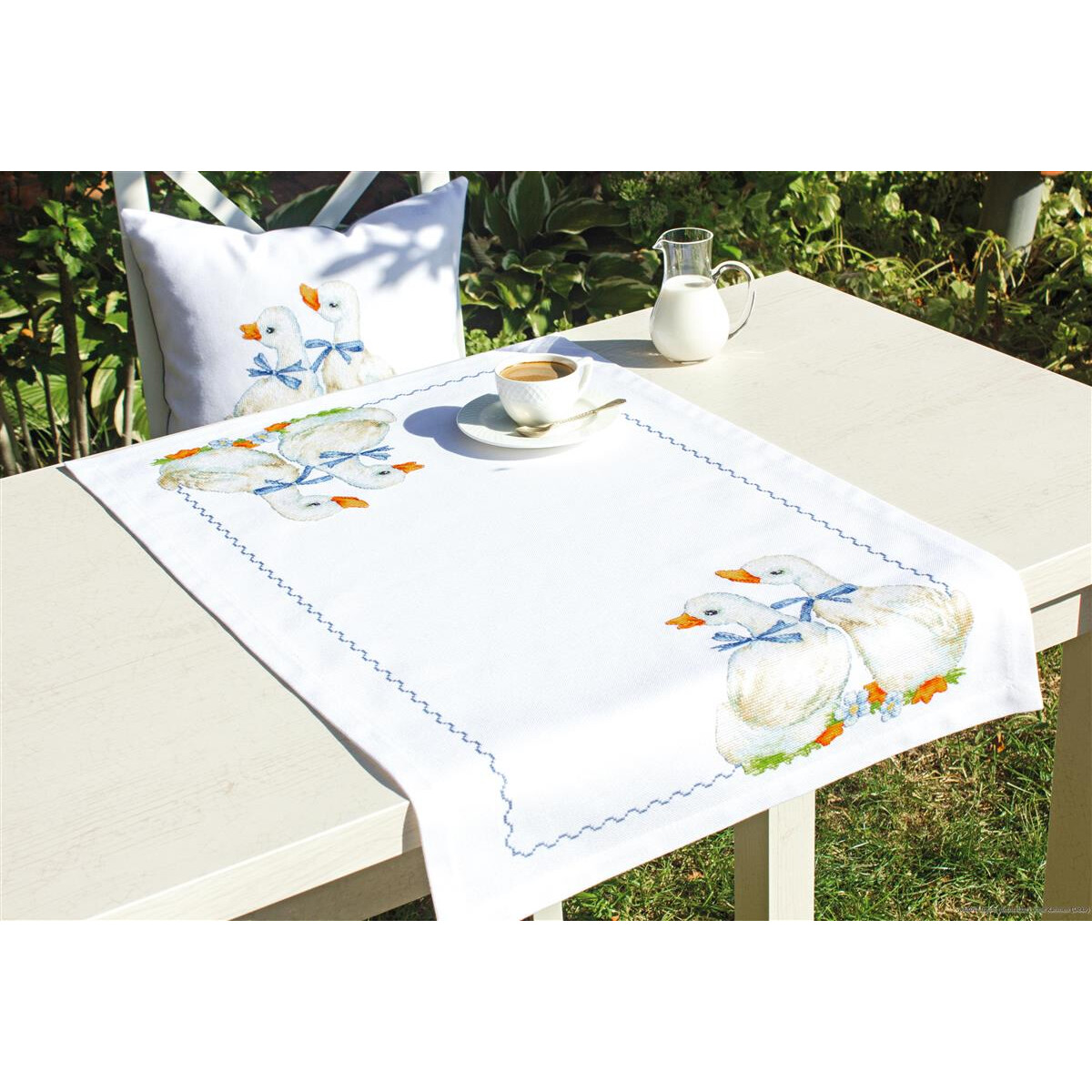 A white tablecloth and a matching cushion, both decorated...