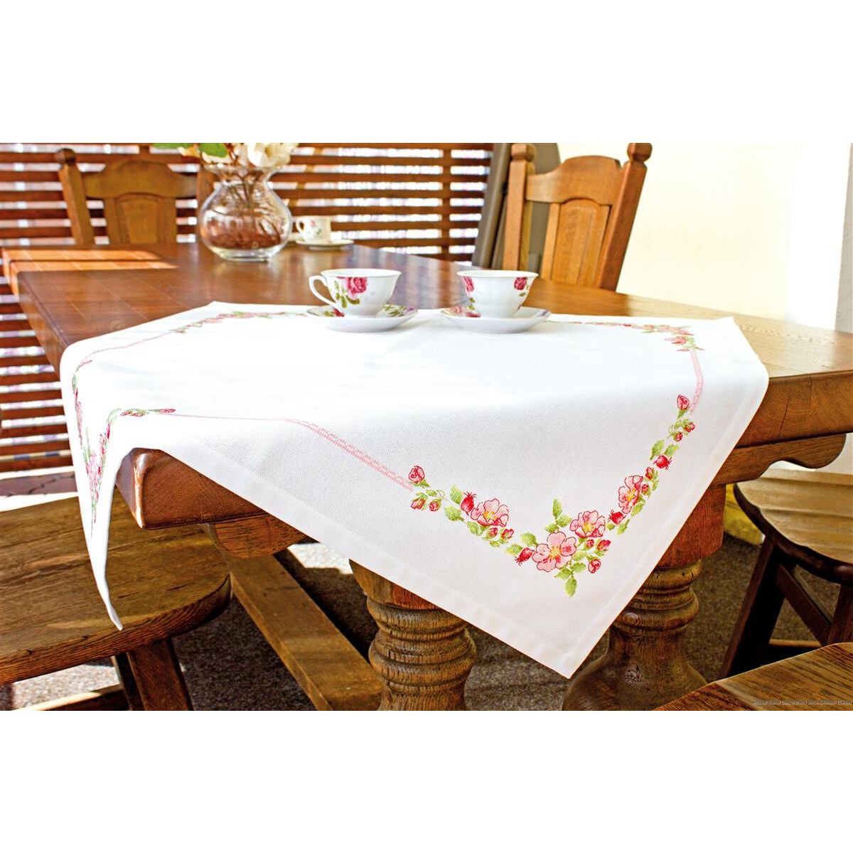 A wooden dining table with a white tablecloth embroidered...