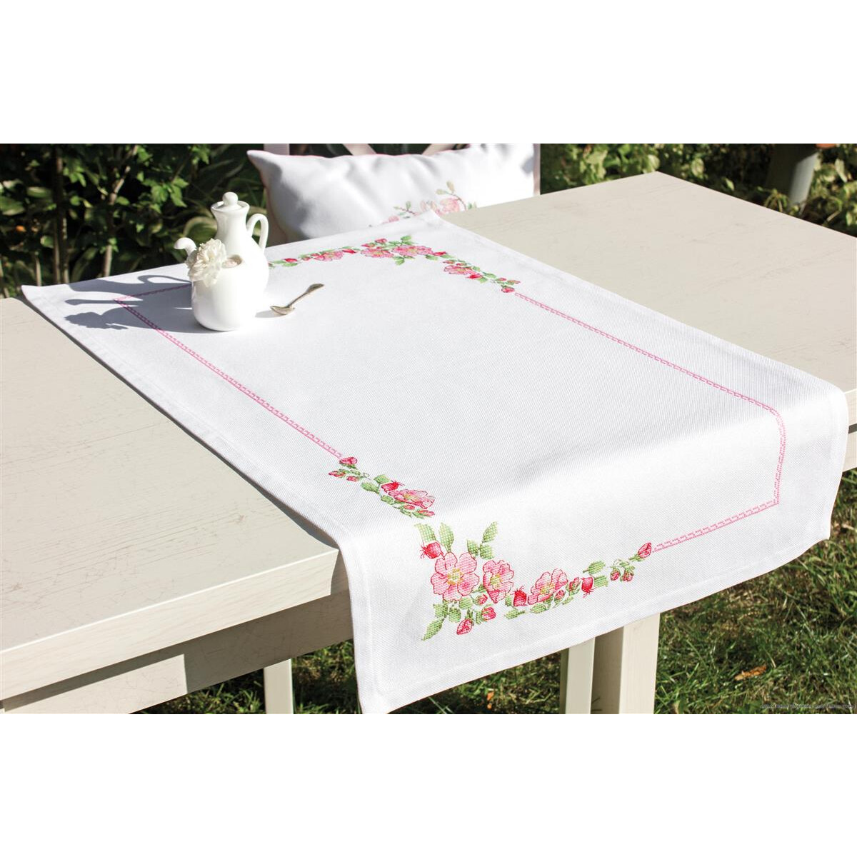 Белый стол на лужайке украшен белой скатертью с вышивкой...