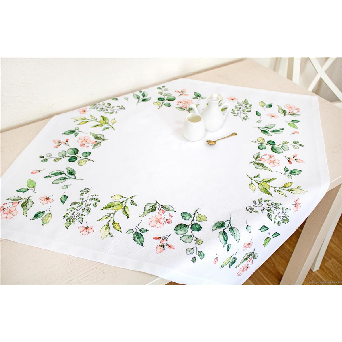 A white tablecloth with floral and leaf patterns on the...
