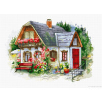 Ein malerisches weißes Häuschen mit steilem grauen Dach, Schornstein und brauner Holzverkleidung. Die Fassade ist mit leuchtenden Blumen geschmückt, darunter rote und rosa Blüten. Der Eingang hat ein schwarzes Geländer, eine rote Tür und einen roten Blumentopf. Eine rote Bank steht neben einem Fahrrad inmitten des üppigen Gartens und ähnelt einem charmanten Design von Lucas Stickpackung. Im Hintergrund sind Bäume zu sehen.