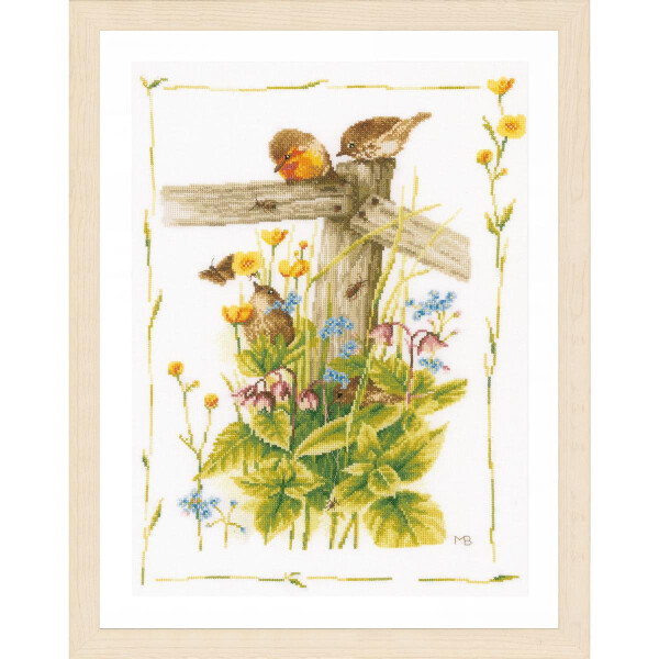 Eine gerahmte Stickpackung von Lanarte zeigt zwei kleine Vögel, die auf einem hölzernen Zaunpfahl sitzen, umgeben von Wildblumen. Leuchtend gelbe Butterblumen, blaue Vergissmeinnicht und andere bunte Blüten füllen die Szene. Eine Biene schwebt in der Nähe der Blumen. Die Initialen des Künstlers „MB“ sind in die untere rechte Ecke gestickt.
