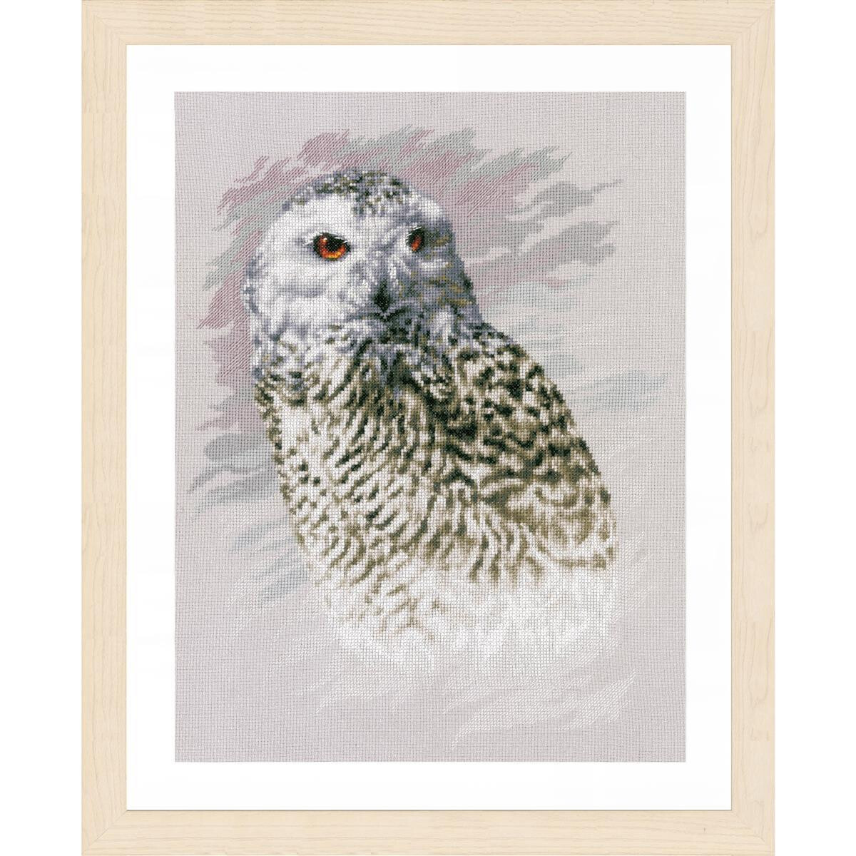 A framed cross stitch artwork of a snowy owl. The owl is...