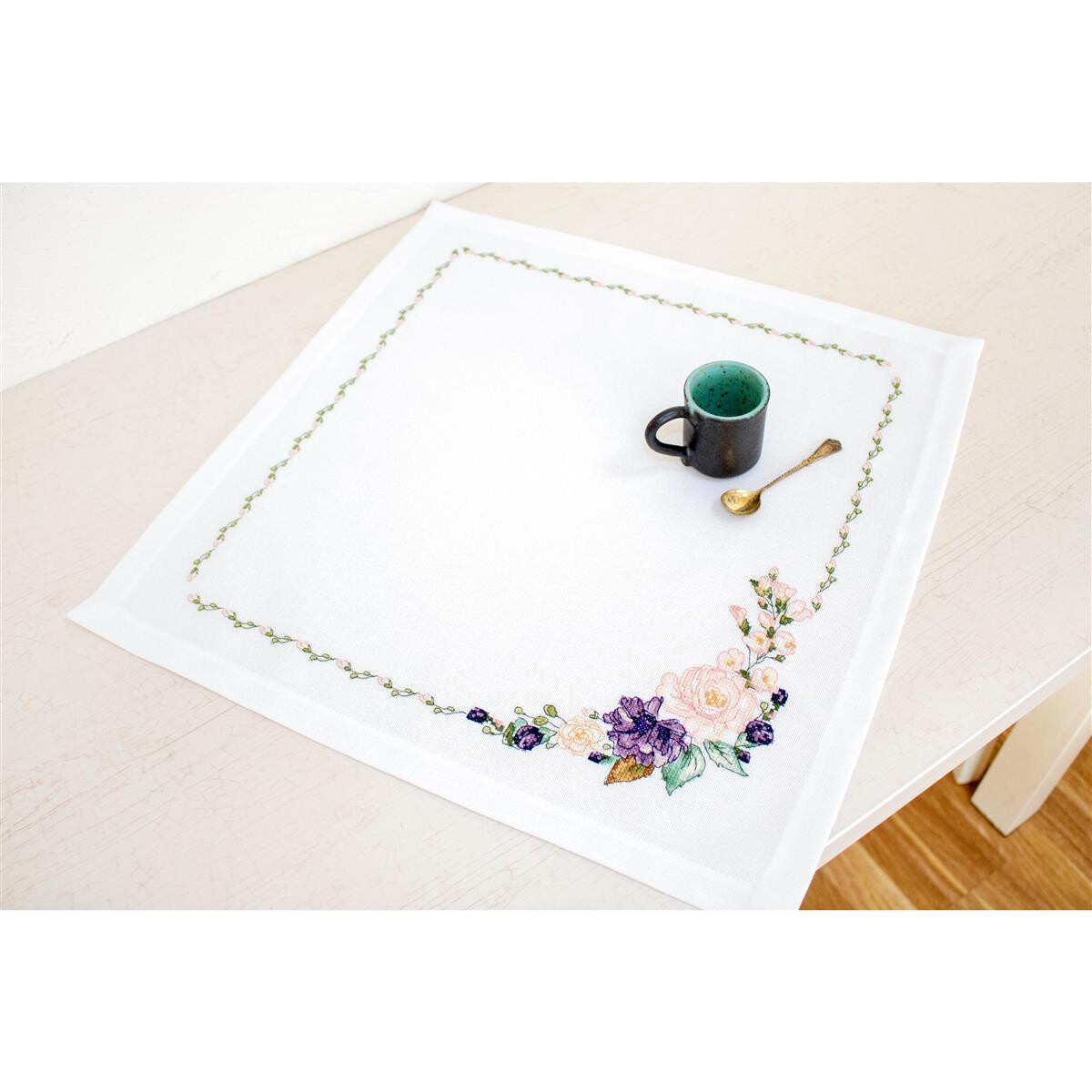 A square white tablecloth with an embroidered border of...