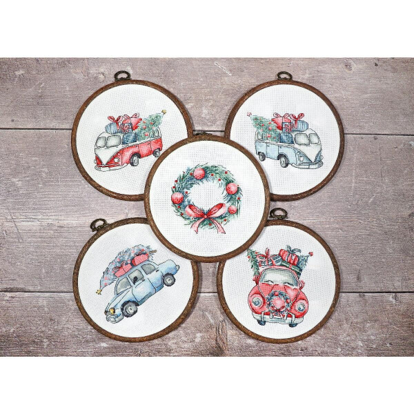 Five round embroidery frames are displayed on a wooden surface. Four frames show vintage cars decorated with Christmas presents and trees on their roofs. The middle frame, an embroidery pack by Letistitch, shows a festive wreath decorated with red bows and berries, on which two red cardinals sit.