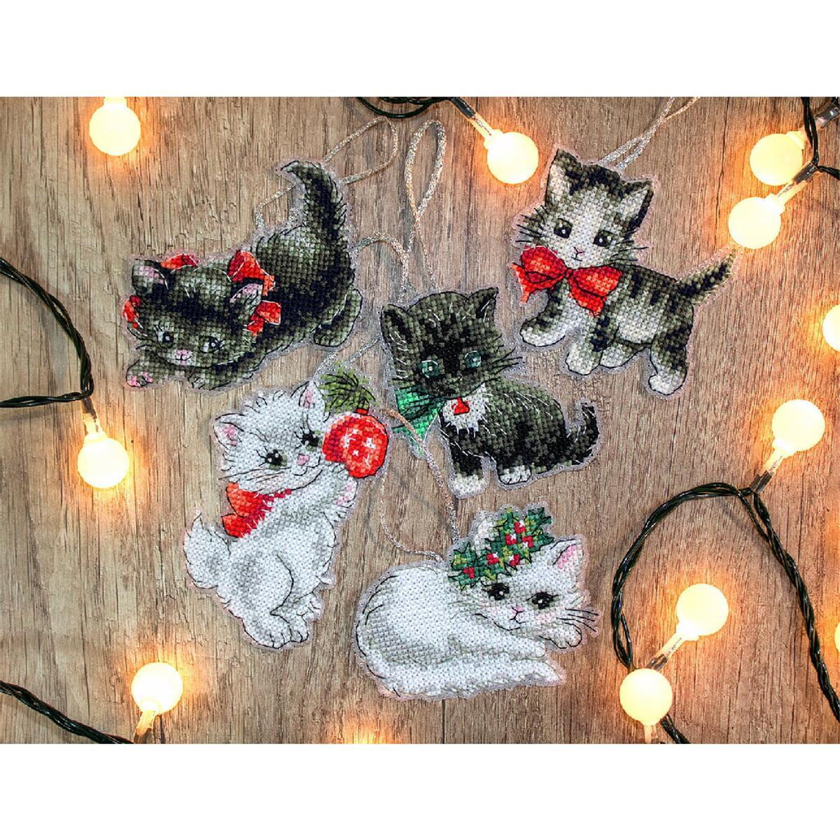 Five cat ornaments decorated with cross-stitch lie on a...
