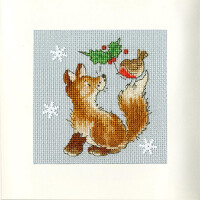 An embroidery pack image from Bothy Threads shows a seated brown fox looking up at a small red-breasted bird sitting on its tail. The bird is holding a sprig of holly. The background is light blue with three white snowflake patterns. This enchanting cross-stitch scene is framed by a white border.