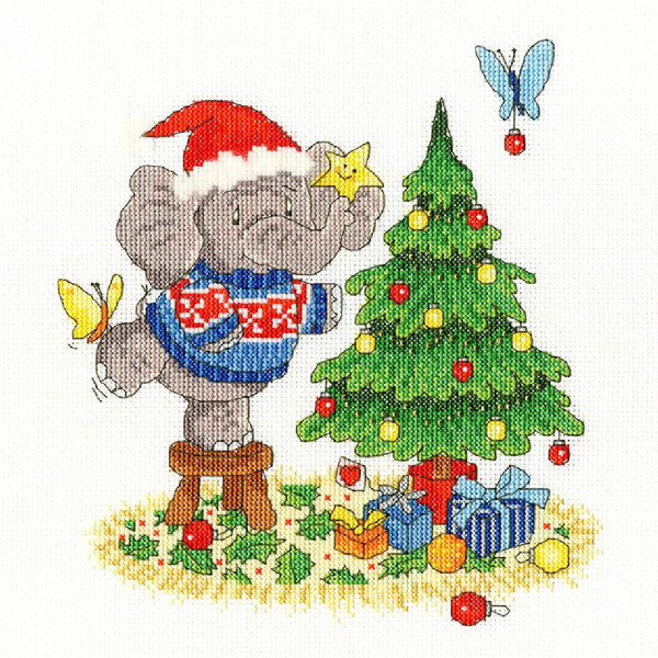 Ein Kreuzstichbild einer festlichen Szene zeigt einen grauen Elefanten mit einer roten Weihnachtsmannmütze und einem blauen Pullover. Der Elefant hängt einen Stern an einen mit Ornamenten und Lichtern geschmückten Weihnachtsbaum. Unter dem Baum liegen eingepackte Geschenke und Schmetterlinge fliegen herum. Diese bezaubernde Stickpackung von Bothy Threads ist ein ideales Bastelprojekt für die Feiertage.