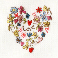 Colorful hand-stitched embroidery on white fabric shows a heart shape made of flowers, leaves and hearts. The word love is embroidered in the center in red, surrounded by various motifs in blue, green, purple, pink and red threads. This embroidery pack from Bothy Threads creates a vibrant, whimsical pattern.
