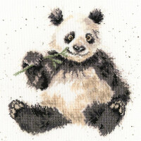 Die Bothy Threads Stickpackung oder das Stickbild zeigt einen süßen Panda, der aufrecht sitzt und einen Bambusstab hält. Das schwarz-weiße Fell des Pandas ist mit detaillierten Kreuzstichen gestaltet und er hat einen liebenswerten Gesichtsausdruck mit großen Augen. Der Hintergrund ist ein spärliches Weiß mit kleinen, zufälligen Flecken.
