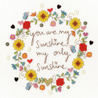 Bothy Threads embroidery pack with the phrase You are my Sunshine, my only Sunshine in the center. Surrounding the text is a floral border with sunflowers, red roses, butterflies and small hearts in several colors. The cross-stitch pattern is applied to a white fabric background.