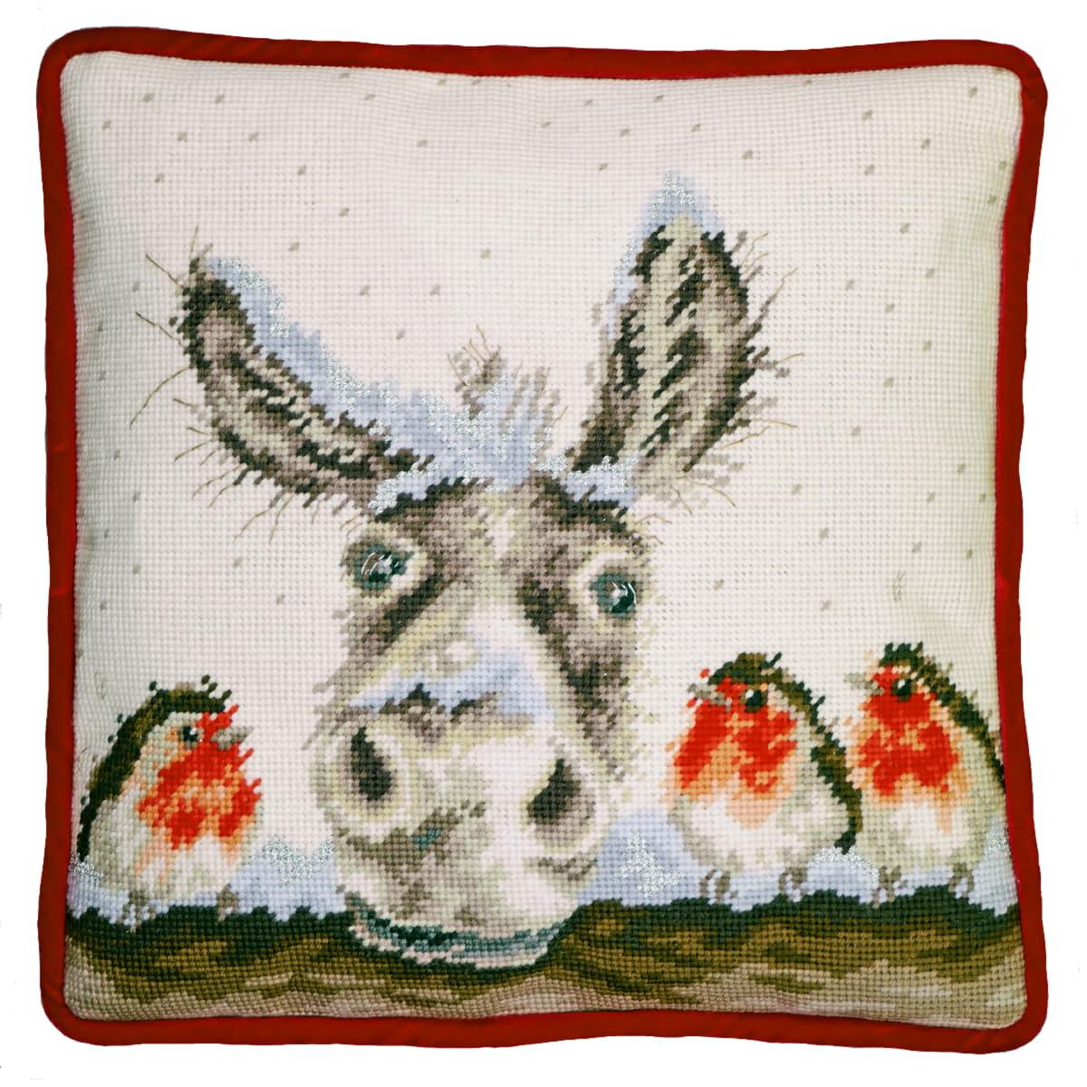 A square cushion with a red border shows a cross-stitch...