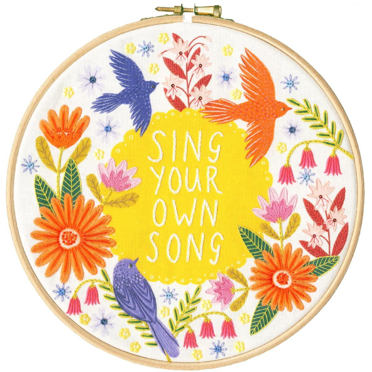 An embroidery hoop shows a lively design with colorful...