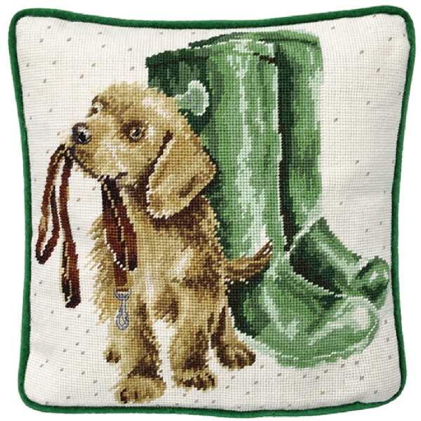 Un paquete de bordados de Bothy Threads con la imagen bordada de un cachorro marrón con una correa en la boca. El cachorro está sentado delante de unas botas de agua verdes, sobre un fondo con pequeños puntos verdes y un borde verde.