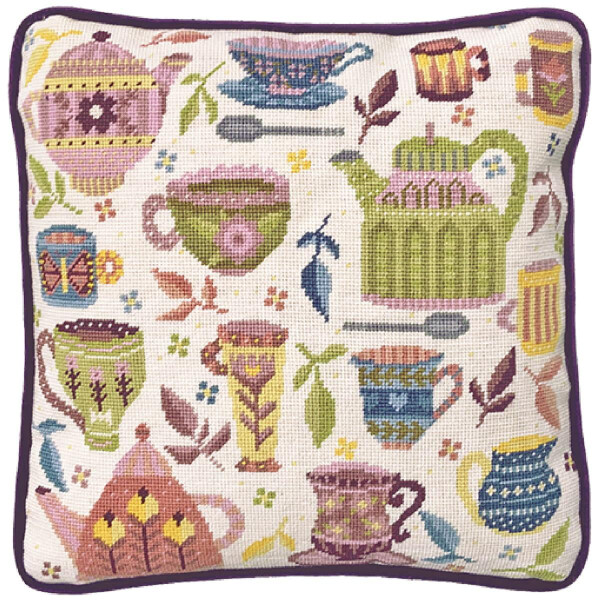 A square cushion with a whimsical tea design reminiscent of a charming Bothy Threads embroidery pack. The cushion is decorated with various colorful tea items including teapots, cups, mugs, spoons and leaves in pastel shades of pink, green, blue and yellow. The cushion has a dark purple border.