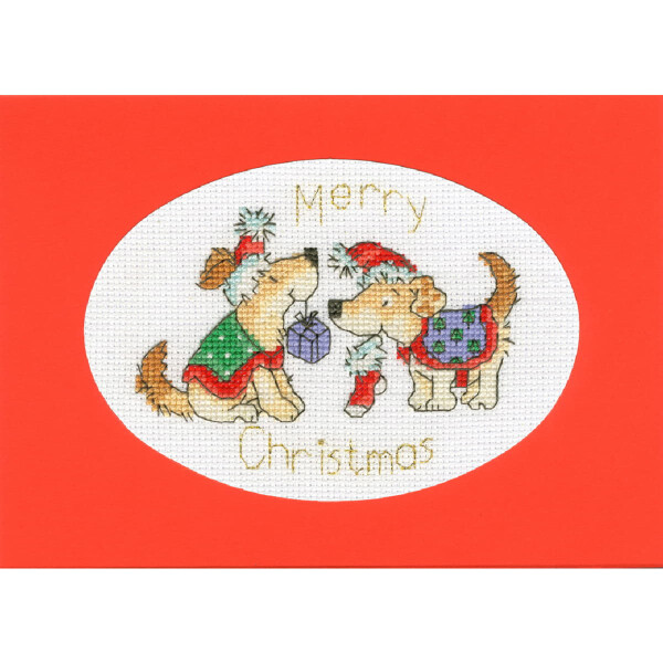 Una festiva tarjeta navideña de punto de cruz de Bothy Threads llamada Embroidery Pack presenta a dos alegres perros con atuendos navideños. Uno lleva un bastón de caramelo en la boca, el otro lleva un gorro de Papá Noel y orejas de reno. Entre ellos hay una caja de regalo. El texto Feliz Navidad está bordado encima y debajo de ellos sobre un fondo rojo.