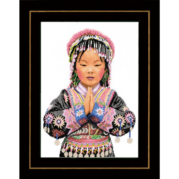 Eine Stickpackung (Lanarte) zeigt ein asiatisches Mädchen in traditioneller Kleidung. Sie hat ihre Hände in einer Gebetshaltung gefaltet und die Augen geschlossen. Ihr Outfit ist mit komplizierten Mustern, Perlen und einem Kopfschmuck mit rosa Akzenten geschmückt. Das Bild ist mit einem schwarzen Rand umrahmt.