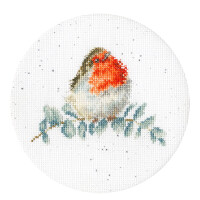 A detailed embroidery pack from Bothy Threads features a cross stitch embroidered robin with a bright red breast and brown and white feathers sitting on a branch. The circular cross-stitch embroidery is arranged on a white background with small, scattered gray dots. Green leaves adorn the branch and add a touch of nature to the scene.