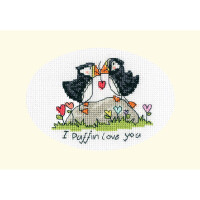 An embroidery pack from Bothy Threads with two puffins sitting close together on a rock. Their beaks are touching and form a heart. The rock is surrounded by colorful flowers. Below the puffins is the text I Puffin love you in black script. The background is a cream-colored oval shape.