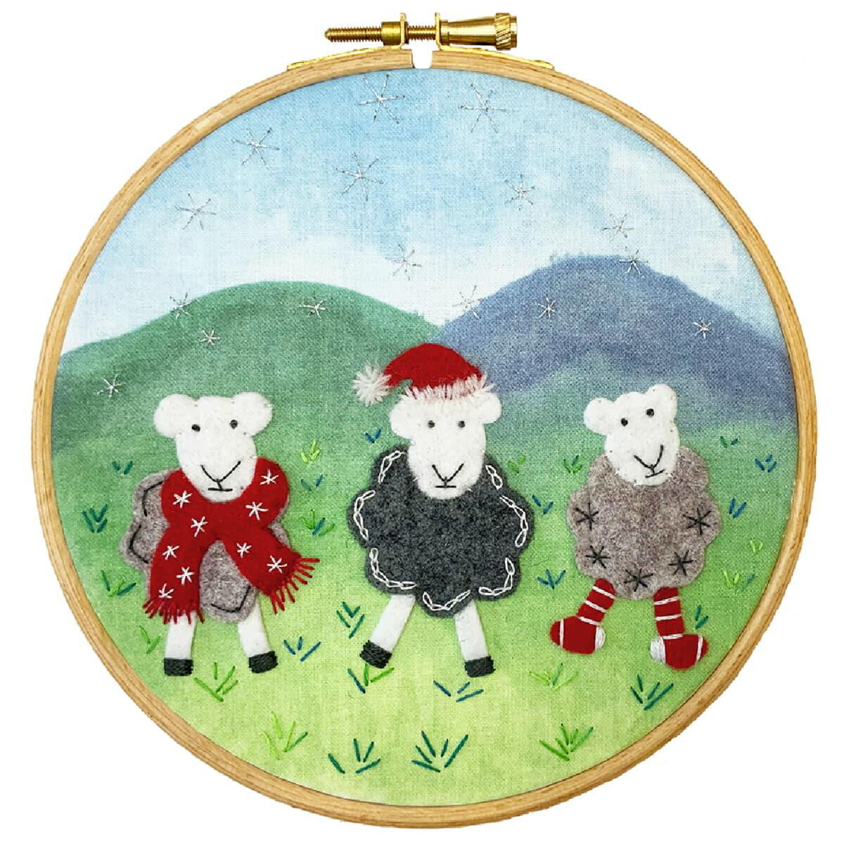 An embroidery frame shows three sheep in a grassy...