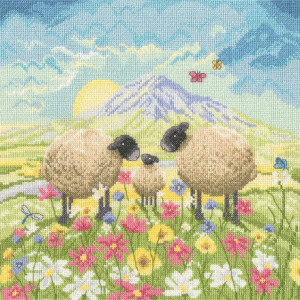 Eine pastorale Stickpackung von Bothy Threads zeigt drei Schafe – zwei größere und ein kleineres – die auf einer lebhaften Wiese voller bunter Blumen stehen. Dahinter sind sanfte Hügel und ein violetter Berg zu sehen, die von der auf- oder untergehenden Sonne beleuchtet werden, während Schmetterlinge unter einem teilweise bewölkten Himmel flattern.