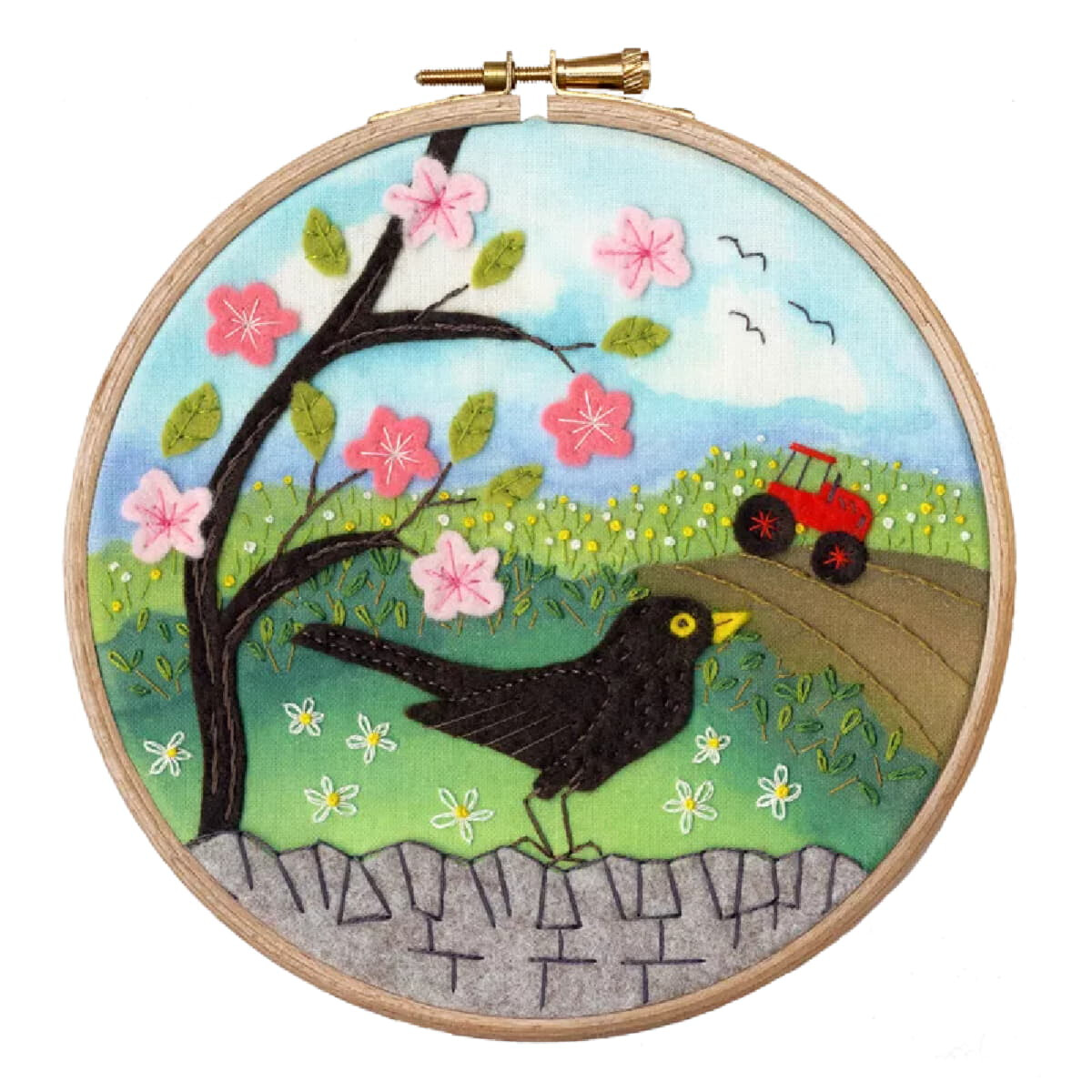 An embroidery hoop shows a lively landscape scene with a...